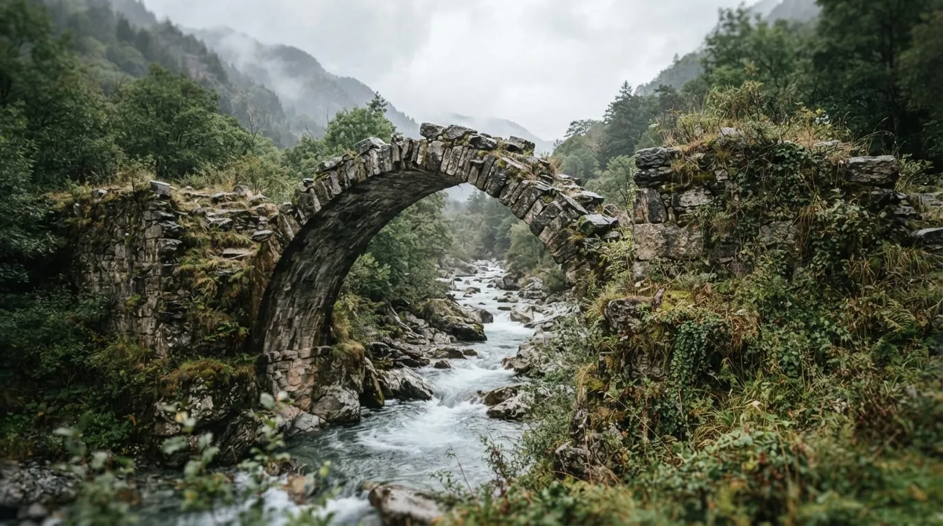 Une arche de pont en pierre brisée au-dessus d’une rivière de montagne, végétation basse sur les culées